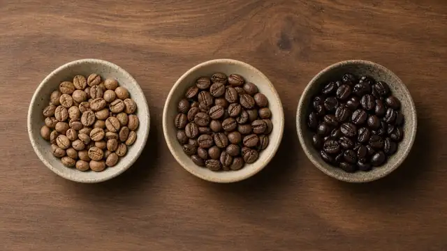 Three bowls of coffee beans showing light, medium and dark roast levels on a walnut table
